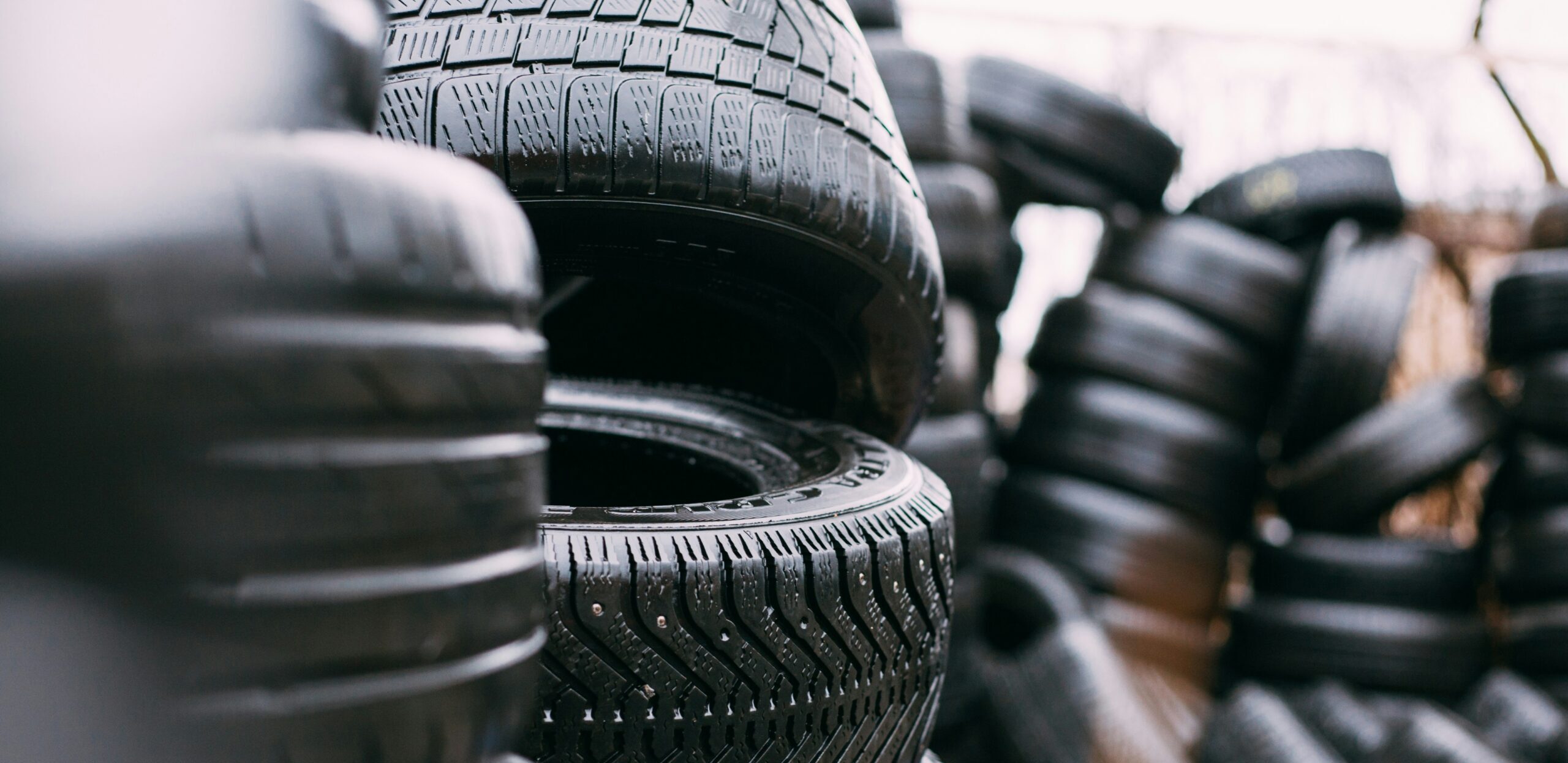 Stack of black car tires with visible tread patterns, photographed outdoors.